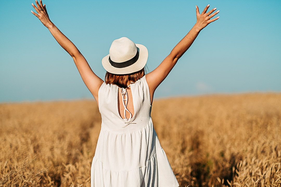 A woman, a girl is standing backwards in a wheat field, her hands raised to the sky. High quality photo