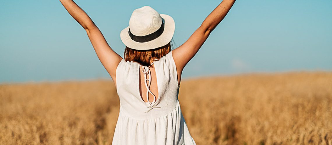 A woman, a girl is standing backwards in a wheat field, her hands raised to the sky. High quality photo